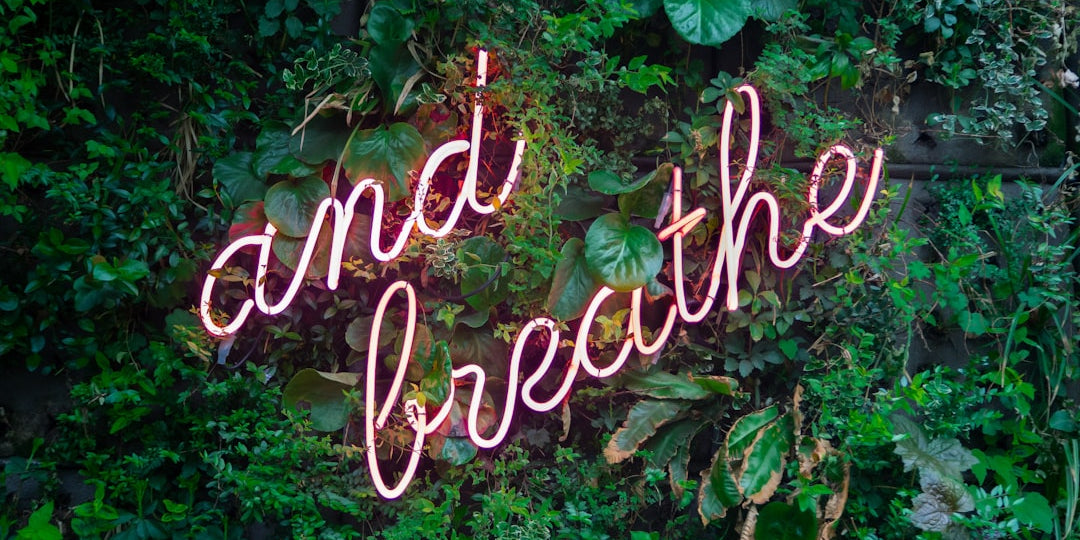 Pink neon sign over greenery with cursive text "and breathe"