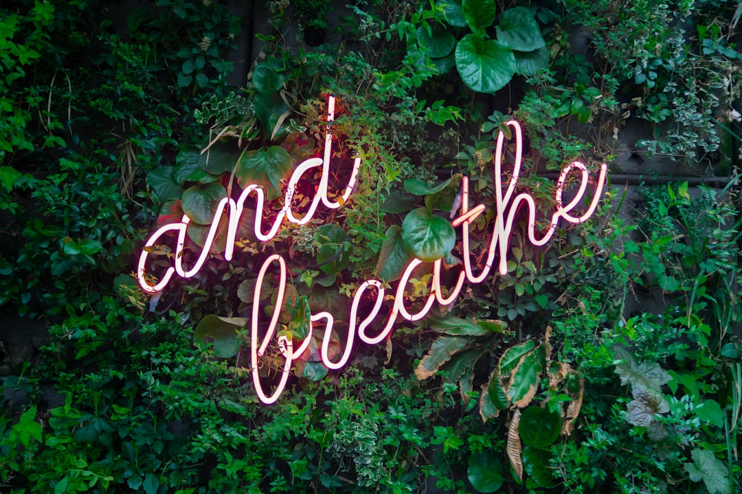 Pink neon sign over greenery with cursive text "and breathe"