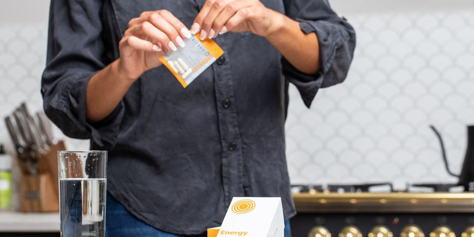 Person opening energy supplement pack by water glass