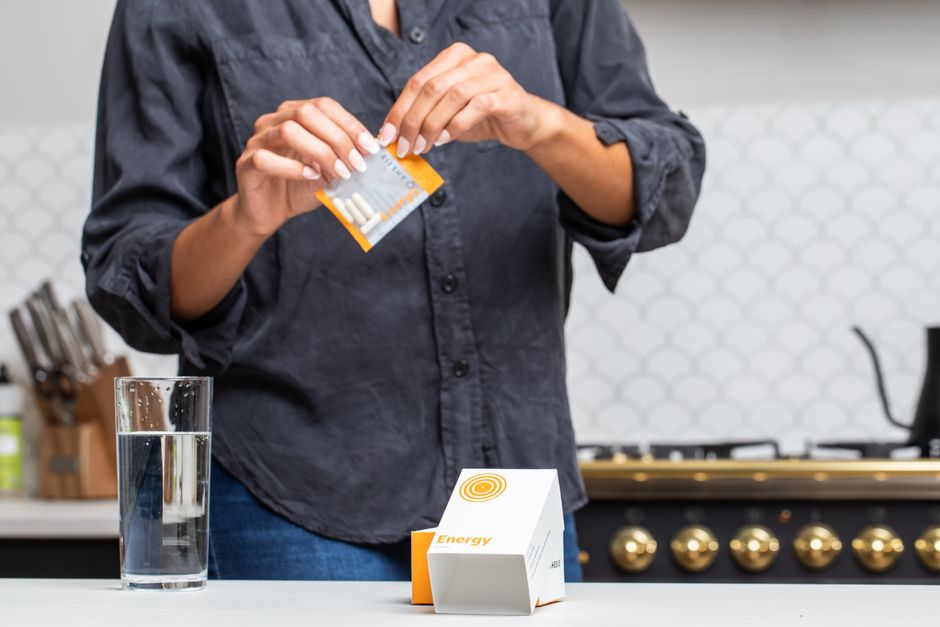 Person opening energy supplement pack by water glass