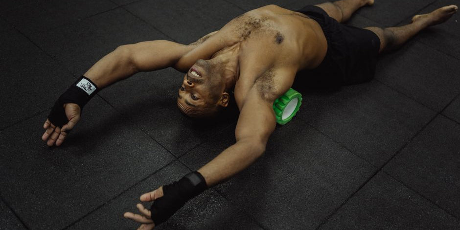 Man using foam roller on black gym floor