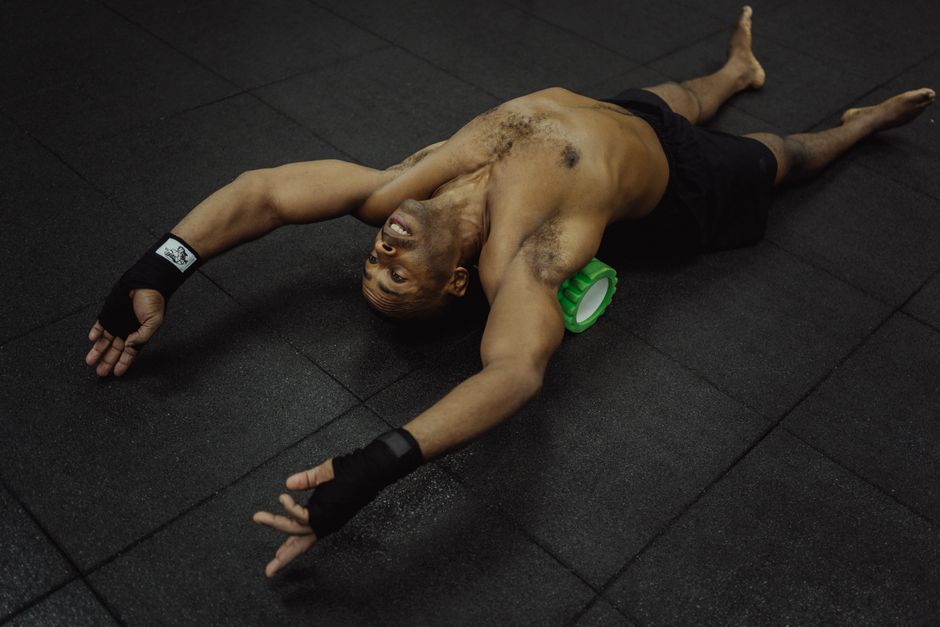 Man using foam roller on black gym floor