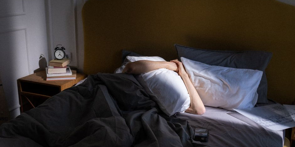 Person covering face with pillow in bed
