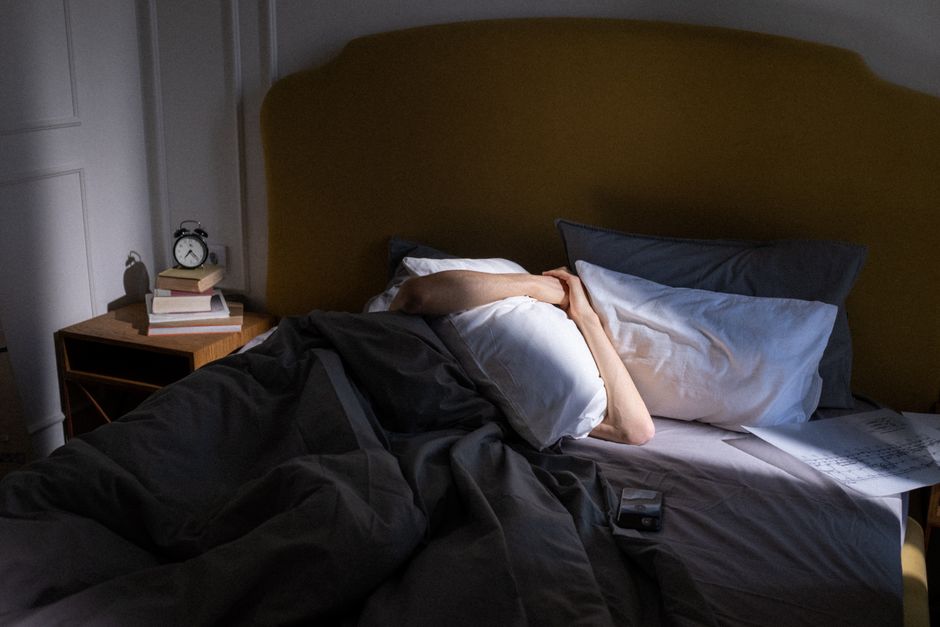 Person covering face with pillow in bed