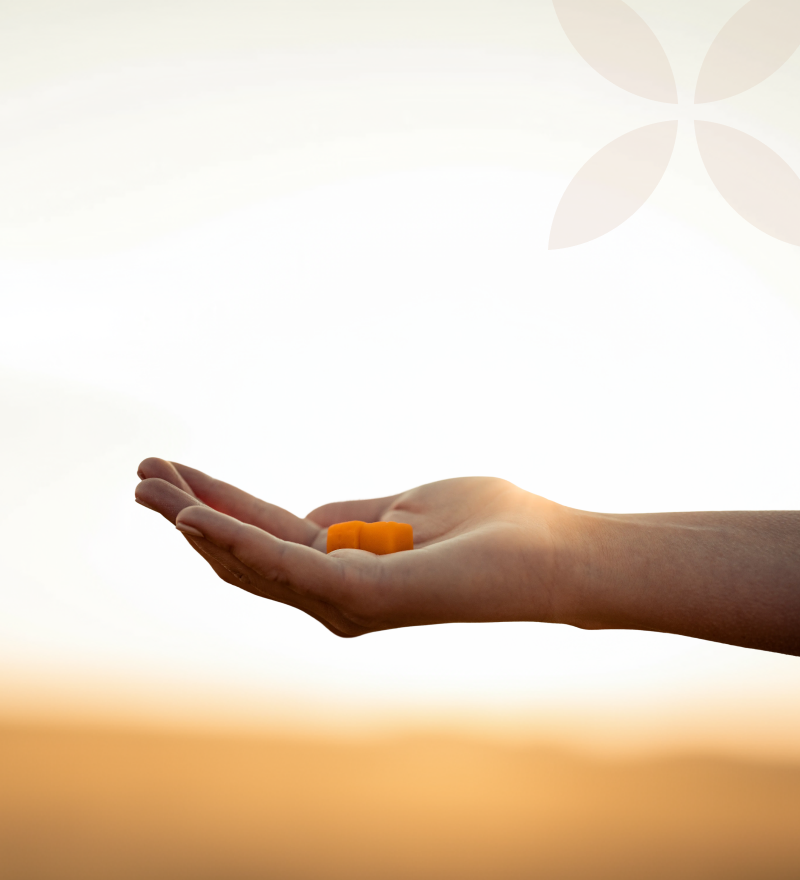Hand holding two orange gummies against a blurred natural background