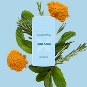 Product Image for Charlotte's Web Balm Stick surrounded by mint leaves, rosemary, and turmeric powder on a blue background