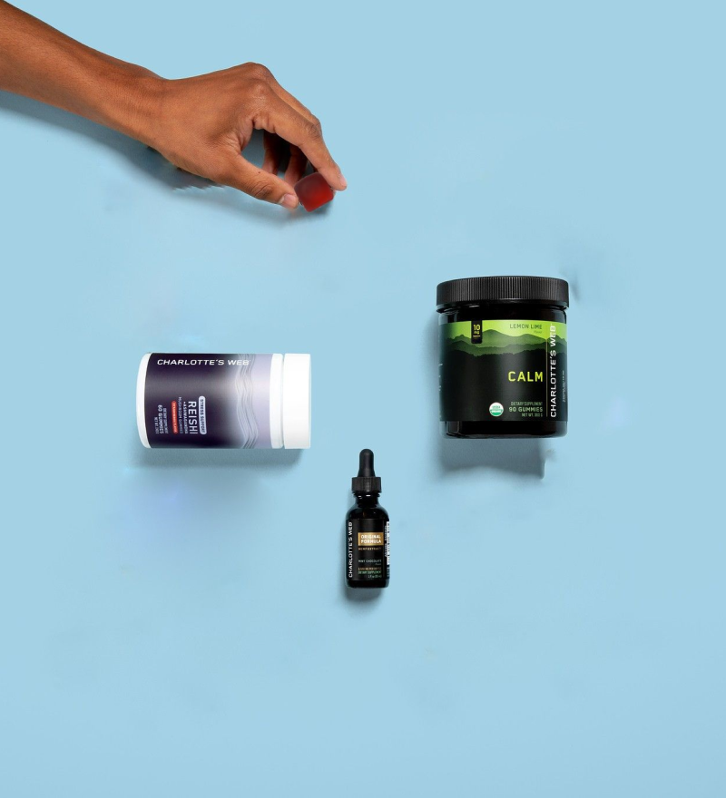 Hand reaching for a bottle of Charlotte's Web on a blue background with other health products.