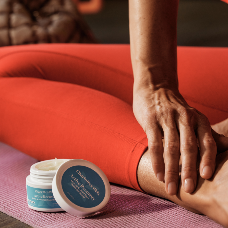 Person applying cream to leg with Chirpfuls Active Recovery jar on pink mat