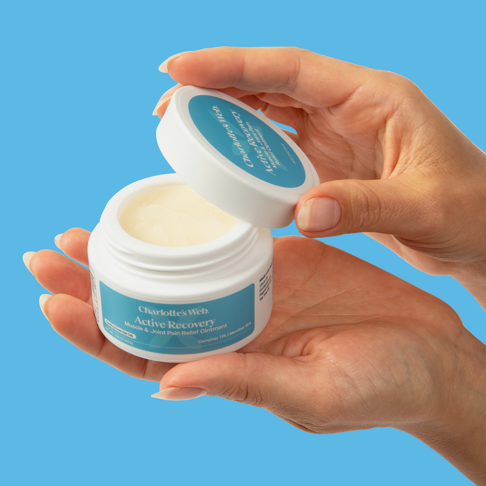 Hand holding a jar of Clarins Active Recovery cream against a blue background