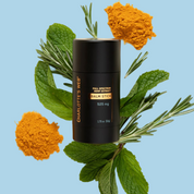 Product Image for Black balm stick with &#39;Charlotte&#39;s Web&#39; branding surrounded by green leaves and orange powder on a light blue background