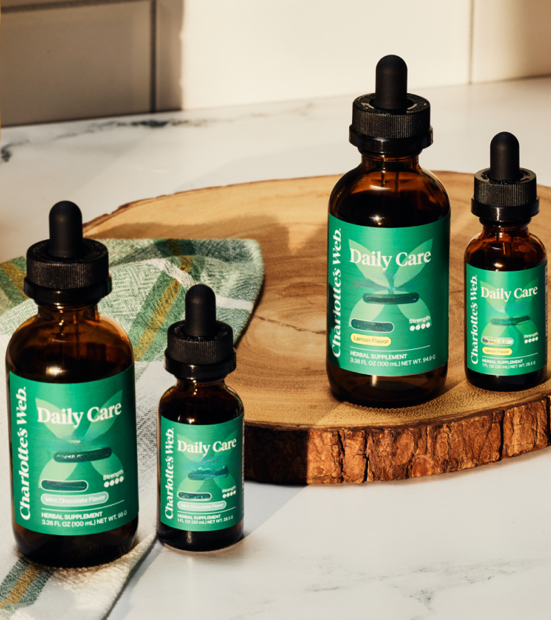 Four bottles of Charlotte's Web Daily Care on a wooden cutting board with a marble countertop background.