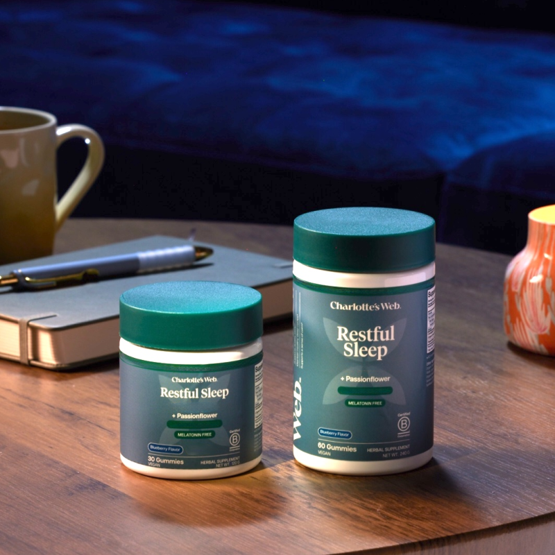 Two containers of Charlotte's Web Restful Sleep supplement on a wooden surface with a blurred background.