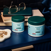Product Image for Two jars of Charlotte&#39;s Web Sleep supplement on a nightstand with books and glasses in the background.