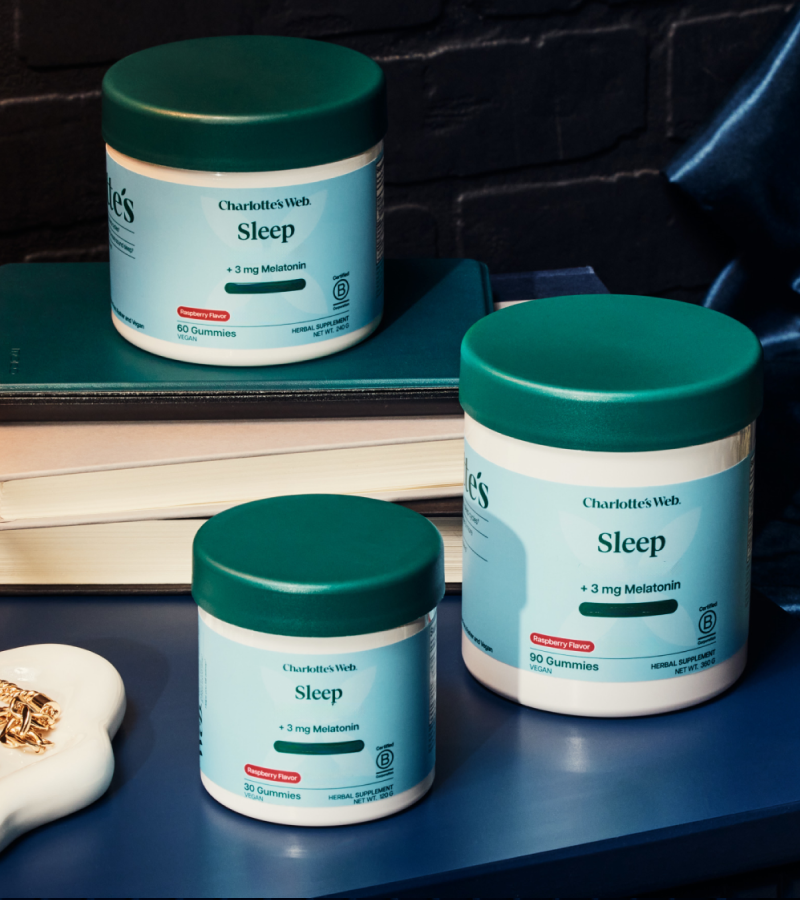 Three containers of Charlotte's Web Sleep gummies on a surface with books in the background.