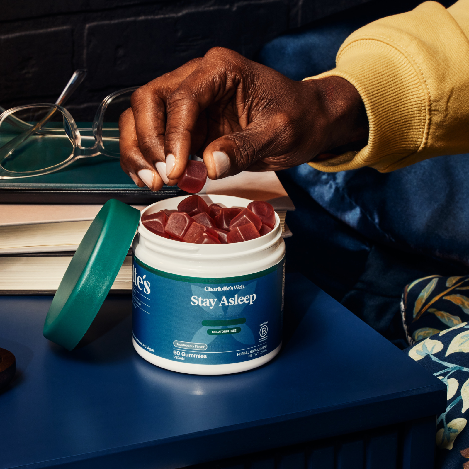 Product Image for Person holding a supplement container labeled &#39;Stay Asleep&#39; with gummy supplements on a desk.