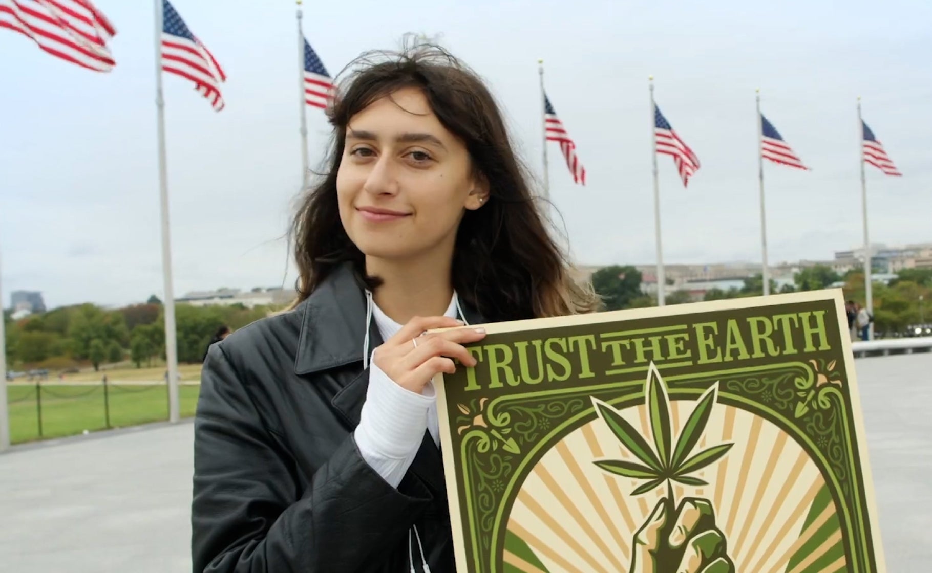 Person holding a sign with a hemp leaf design in front of American flags