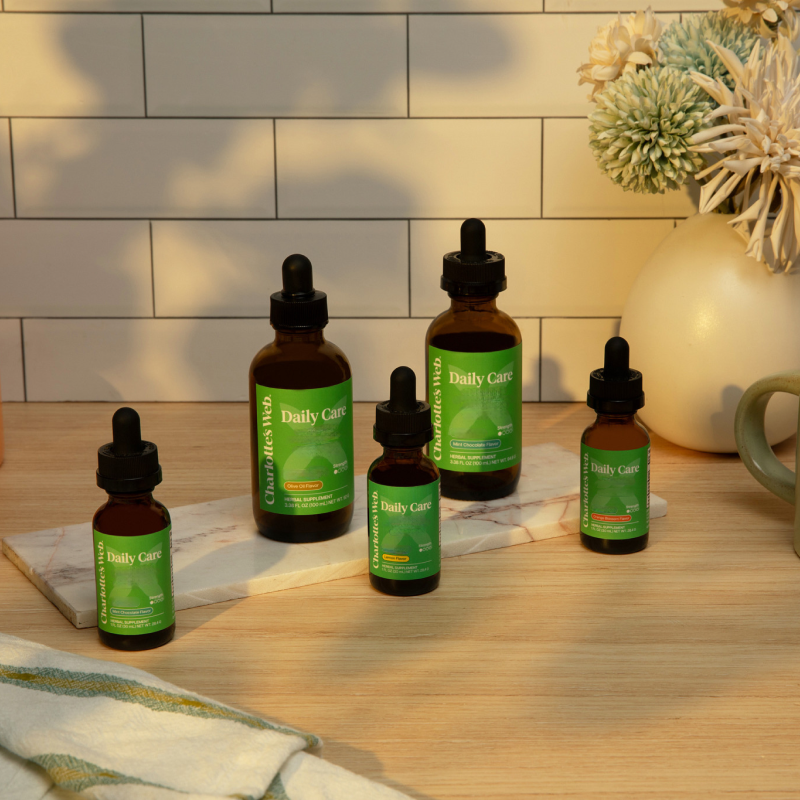 Five bottles of 'Daily Care' on a wooden surface with a tiled wall background.