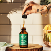Product Image for Hand with a dropper bottle of &#39;Daily Care&#39; on a wooden surface with a tiled wall background.