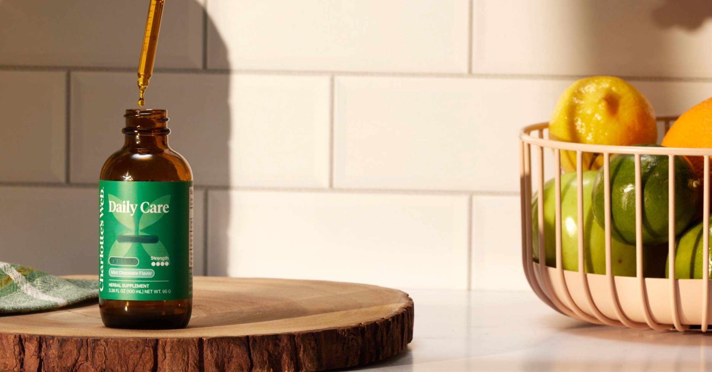 Bottle of Daily Care product with a dropper on a wooden surface next to a basket of fruits.
