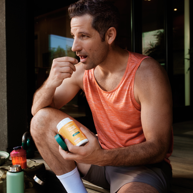 Man in an orange tank top sitting outdoors holding a supplement bottle.