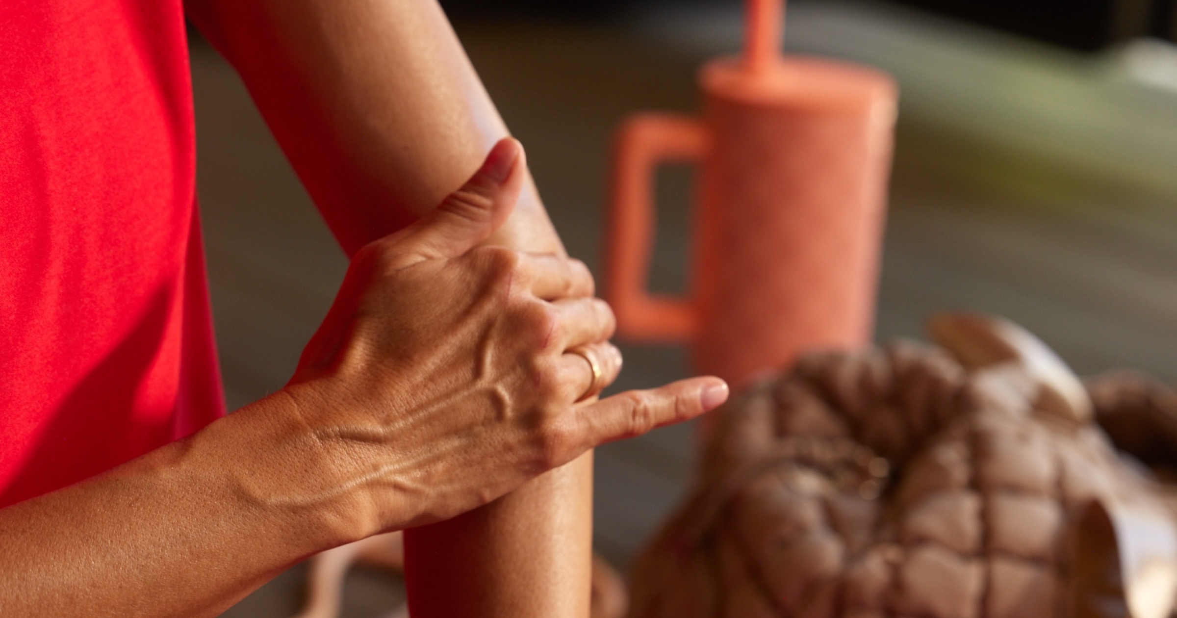 Close-up of a person's hands with a blurred background featuring a red cup and brown object.