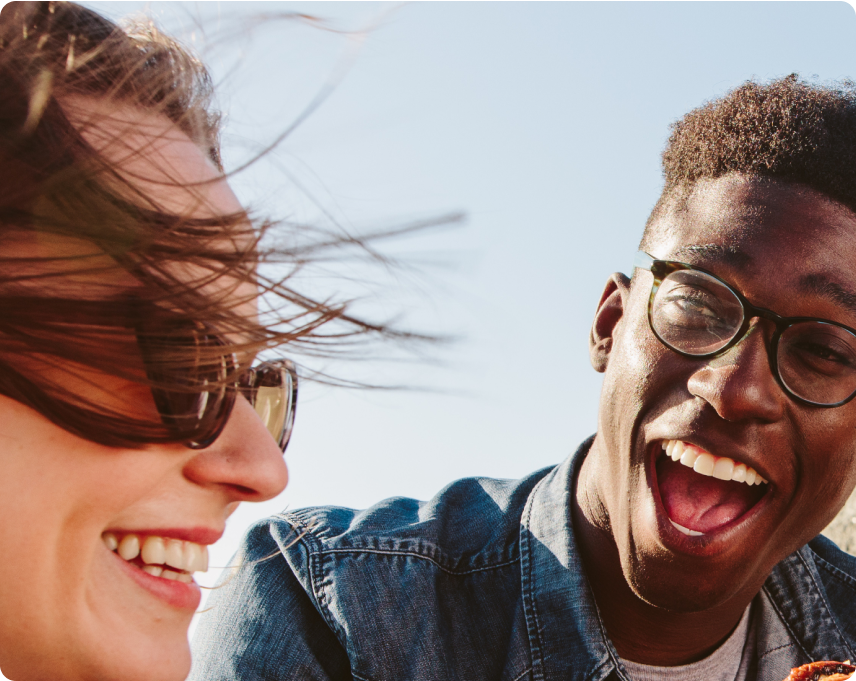 Two people laughing outdoors with a clear blue sky.