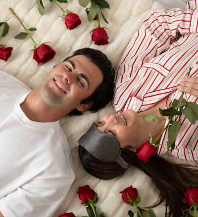 Couple lying on a bed with red roses around them, smiling.