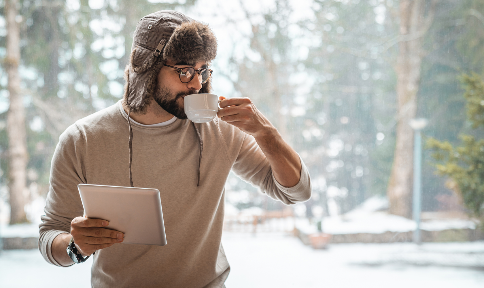 Man in winter clothing drinking coffee and using a tablet in a snowy landscape