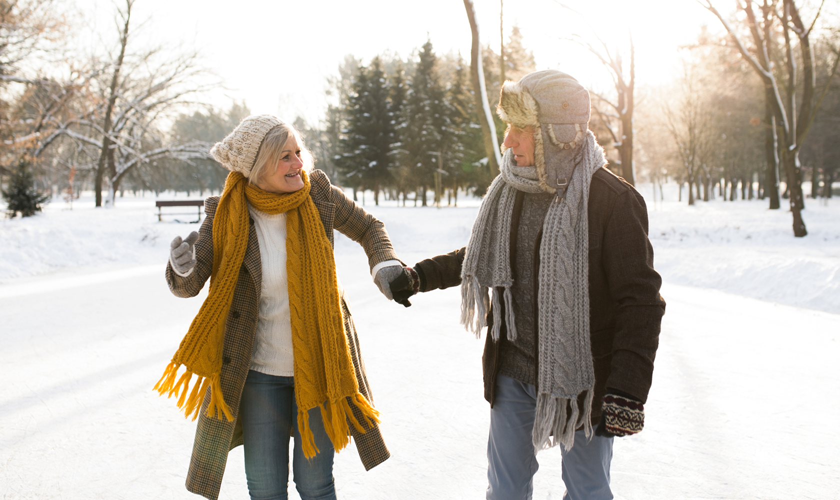 Two people walking hand in hand on a snowy path with trees in the background.