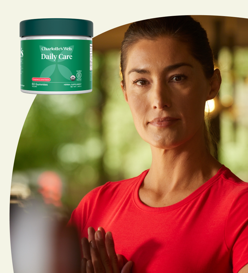 Woman in red shirt with Charlotte's Web Daily Care Gummies jar on a blurred natural background