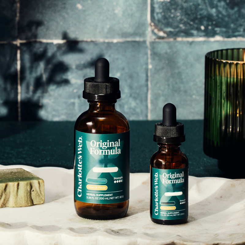 Two bottles of Charlotte's Web Original Formula on a marble surface with a tiled wall background.