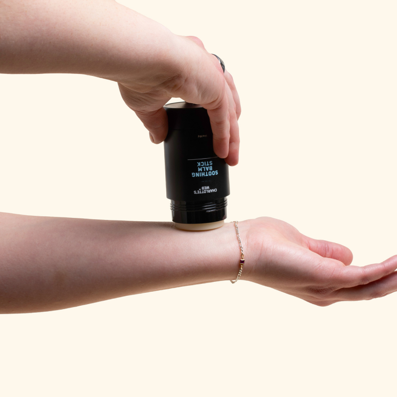 Person applying the soothing balm stick to arm on a cream background