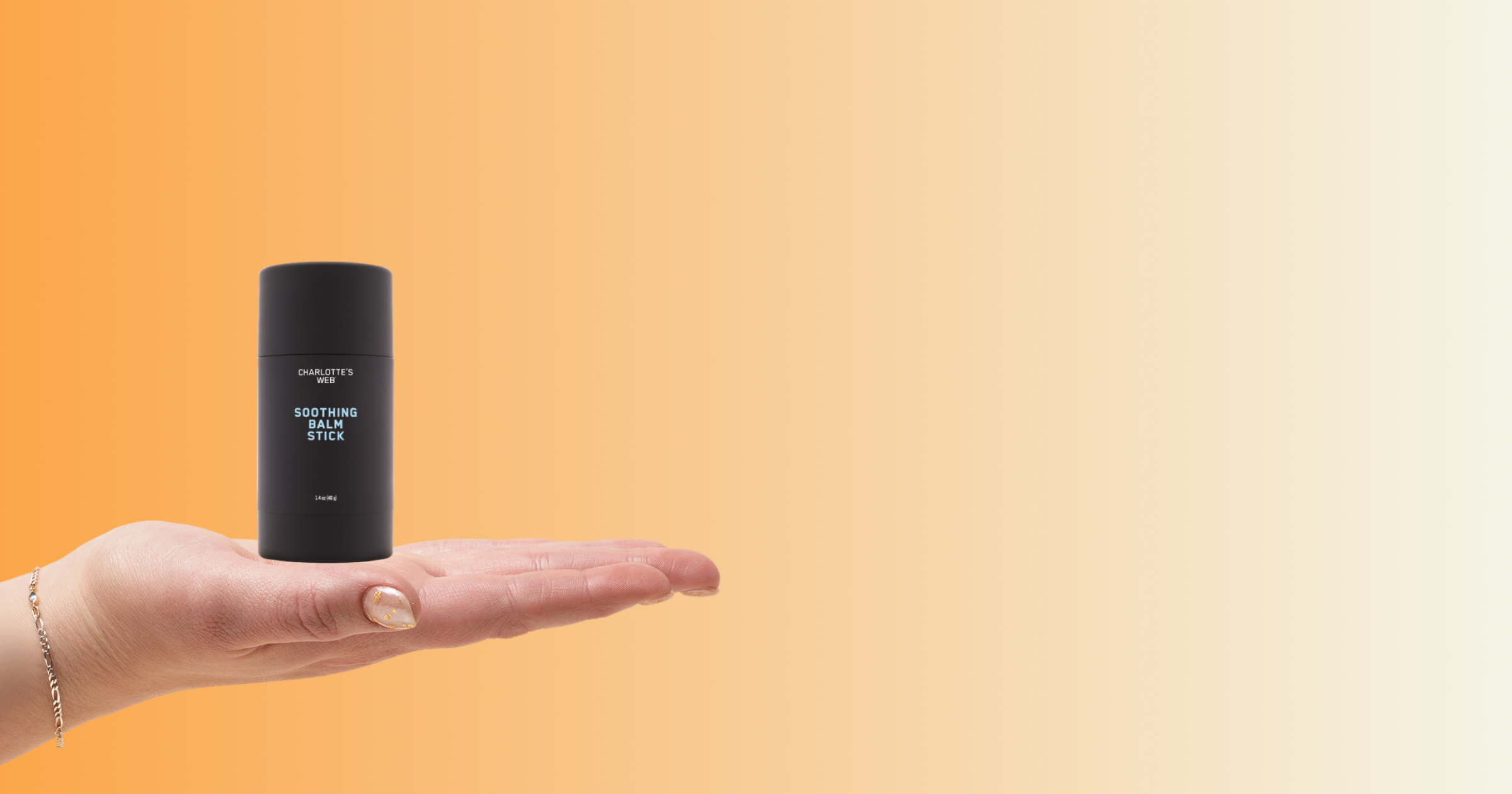 A hand holding a Charlotte's Web Soothing Balm Stick against a warm orange-to-cream gradient background.