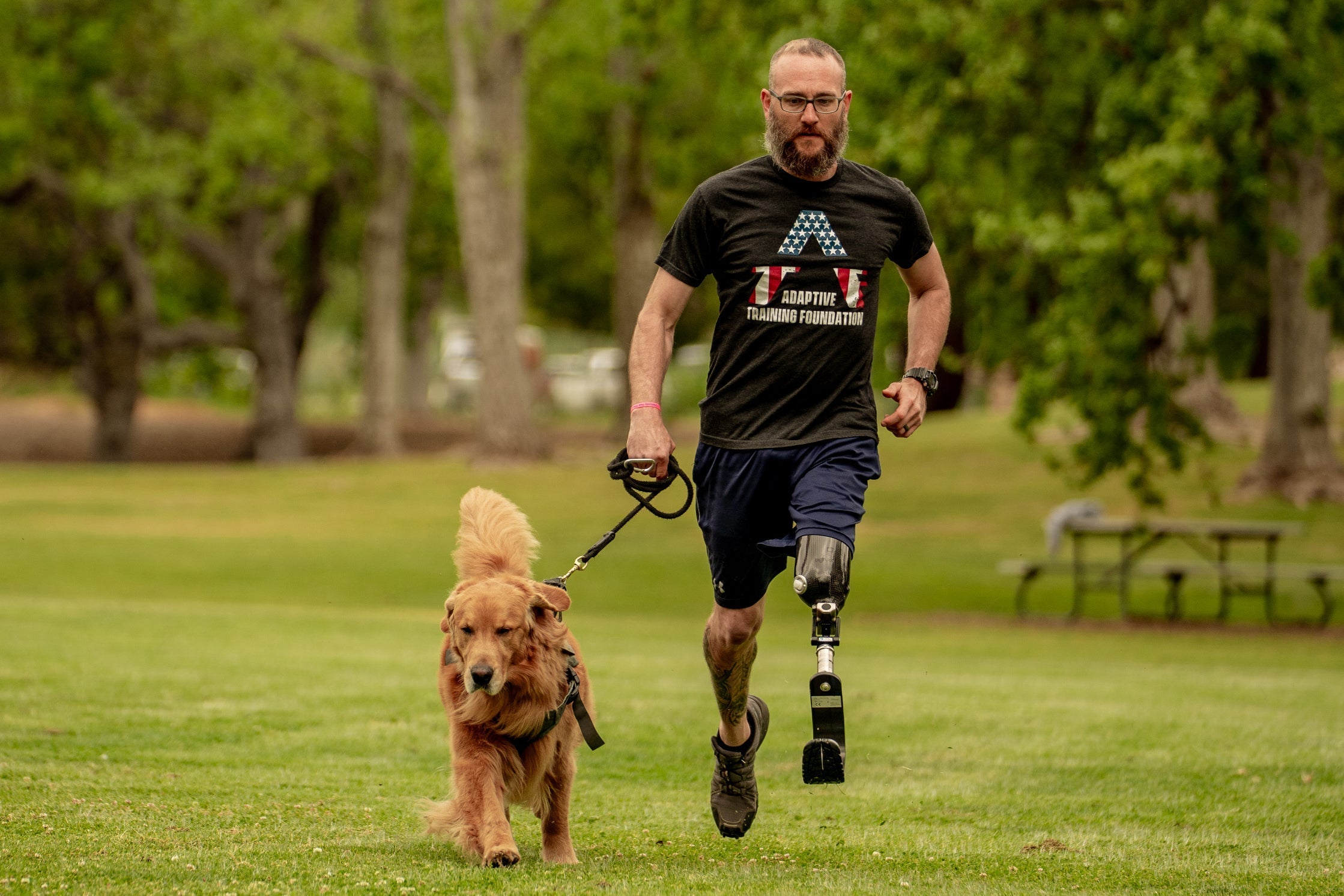 Man with a prosthetic leg running with a dog in a park