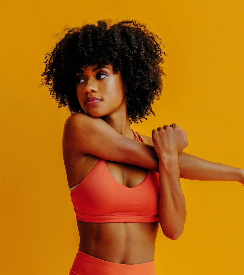 Woman in an orange sports bra and leggings against a yellow background
