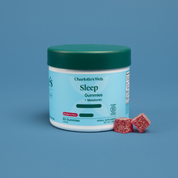 Product Image for Charlotte's Web Sleep Gummies + Melatonin jar with a teal lid and light blue label, shown on a blue background with two red gummy cubes in front.