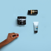 Product Image for Three skincare products on a light blue background with a hand reaching for one of them.