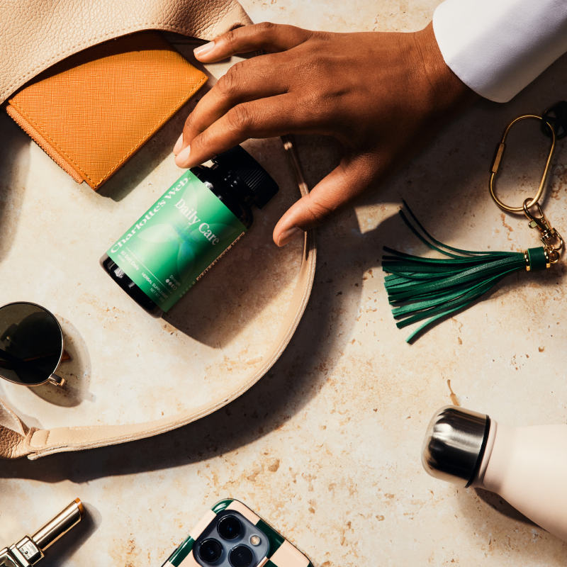 Hand holding a green bottle labeled 'Cypress' on a textured surface with a handbag and other items.