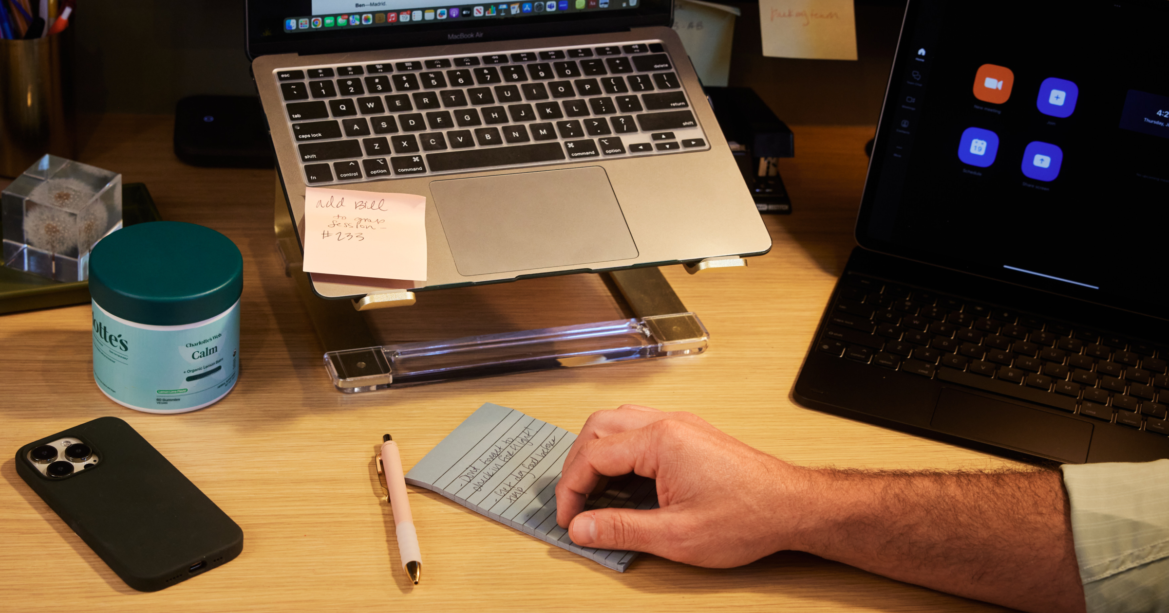 Person using a calculator on a desk with laptops, phone, and other items.