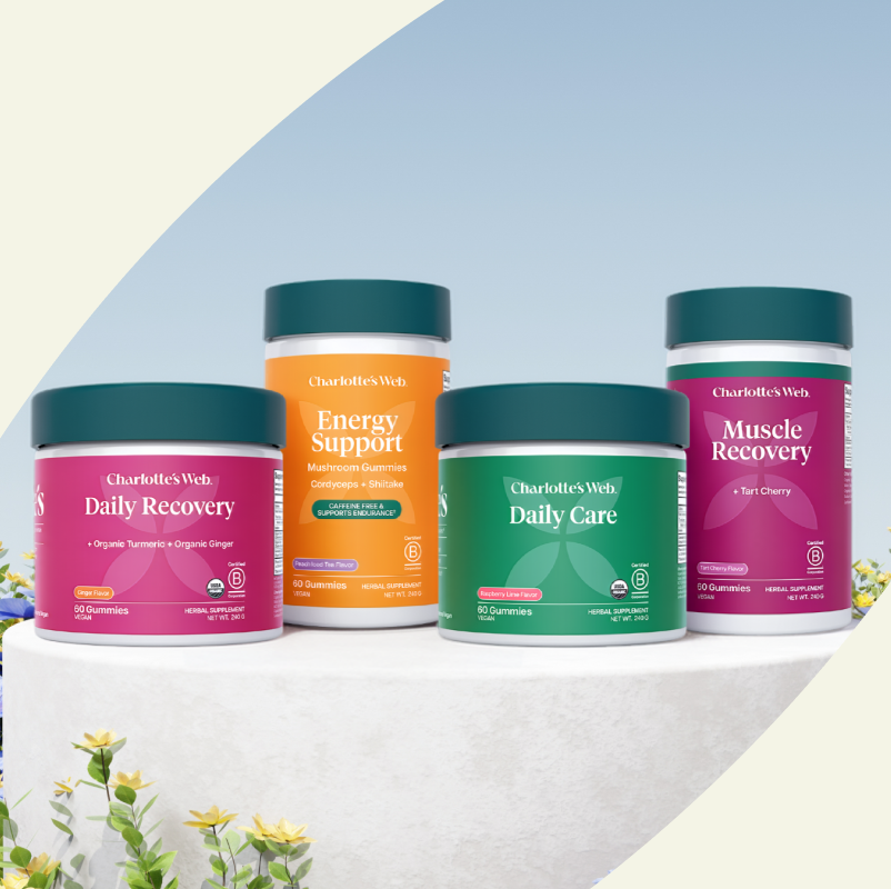 Four containers of Charlotte's Web supplements on a light background with flowers.
